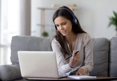 116422466-happy-young-woman-in-headphones-speaking-looking-at-laptop-making-notes-girl-student-talking-by-vide-1