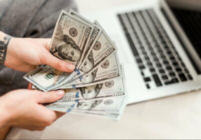 1600951323-close-up-woman-hands-holding-new-dollar-bills-she-earned-working-from-laptop-home-online-97712-81